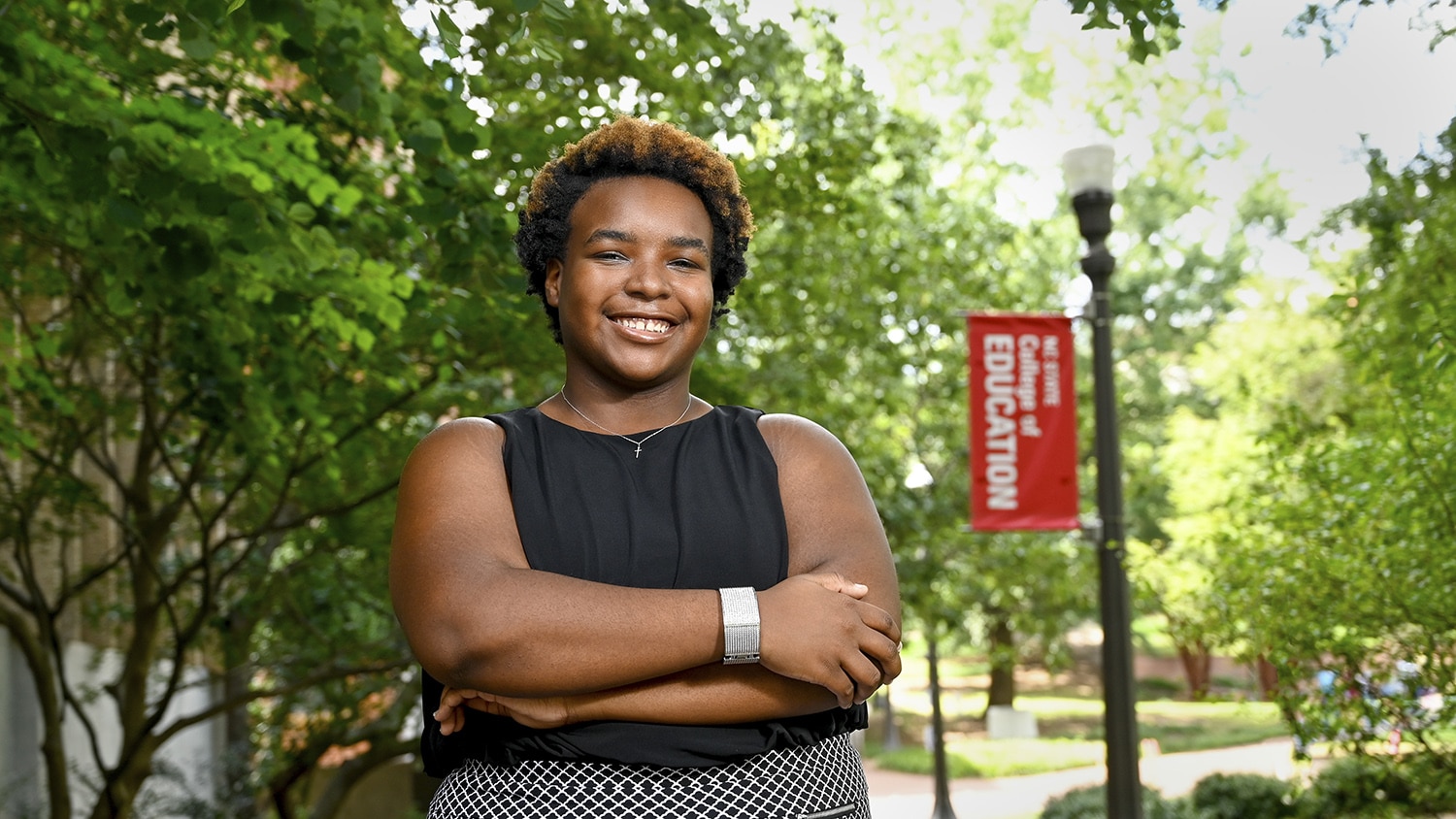 Alycia Morgan is pictured outdoors with a lamp post banner in the background that reads "NC State College of Education".