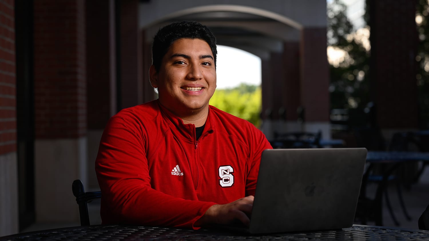 Carlos Alonzo-Montufar is pictured outside the Wilson College of Textiles, seated at a table with a laptop.