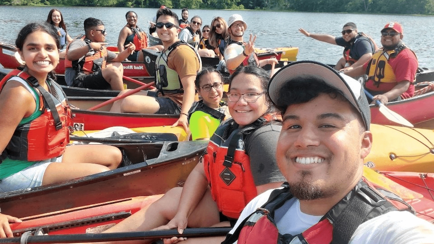 Students and staff smiling into camera as they take a selfie in kayaks on Lake Johnson.