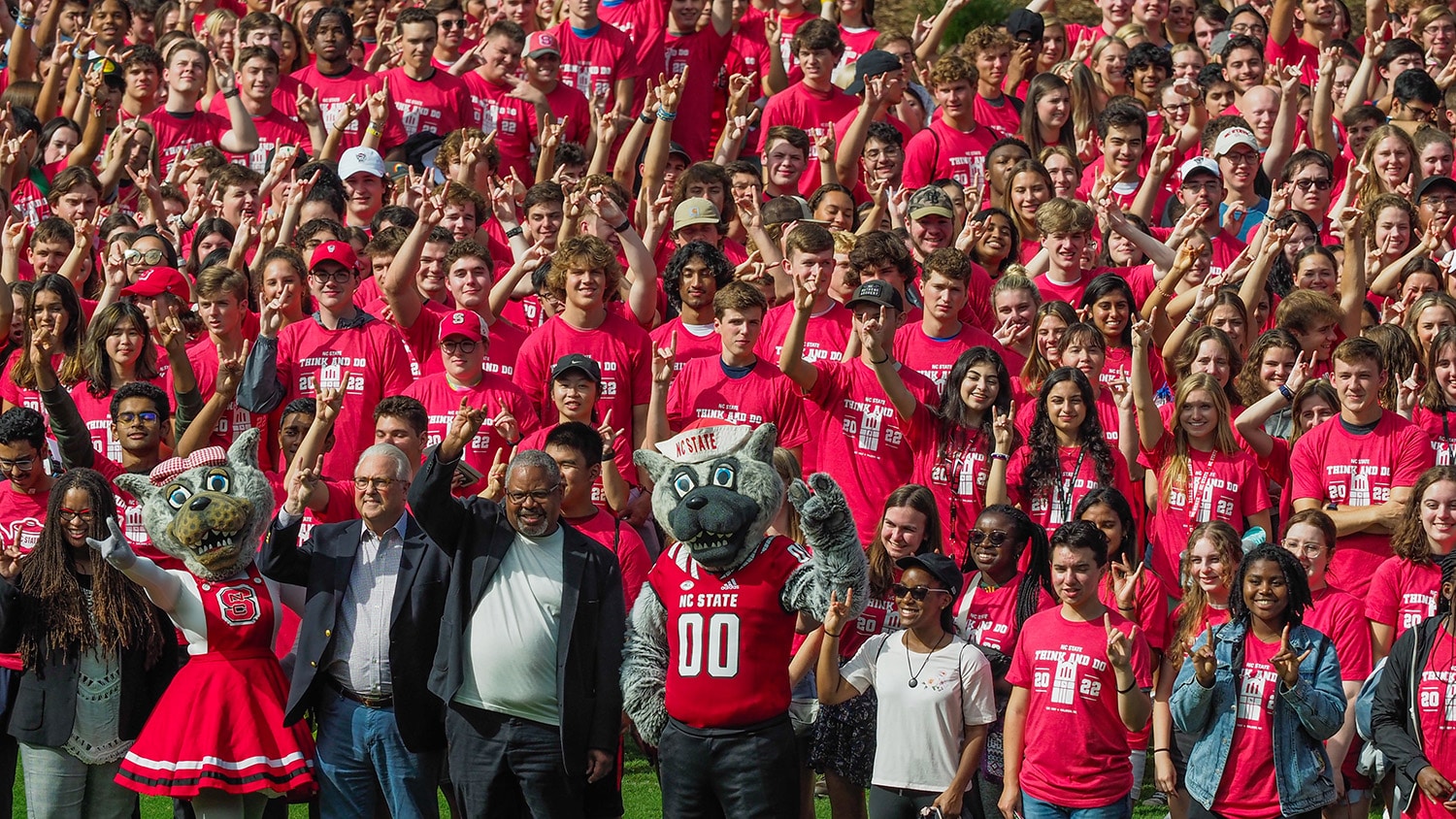 A large group of students wearing matching NC State shirts pose with the Chancellor, faculty members and Mr. and Ms. Wuf for a photo.