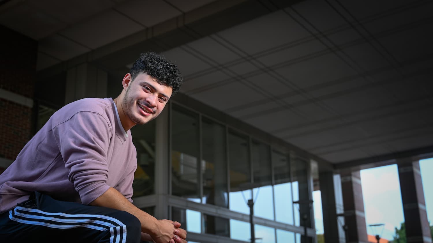 Student seated in front of building leaning forward slightly