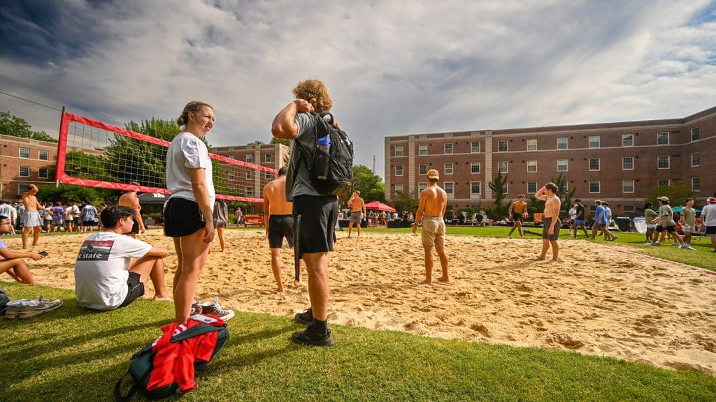 Nestled between residence halls, a large group plays volleyball on a sandy court.