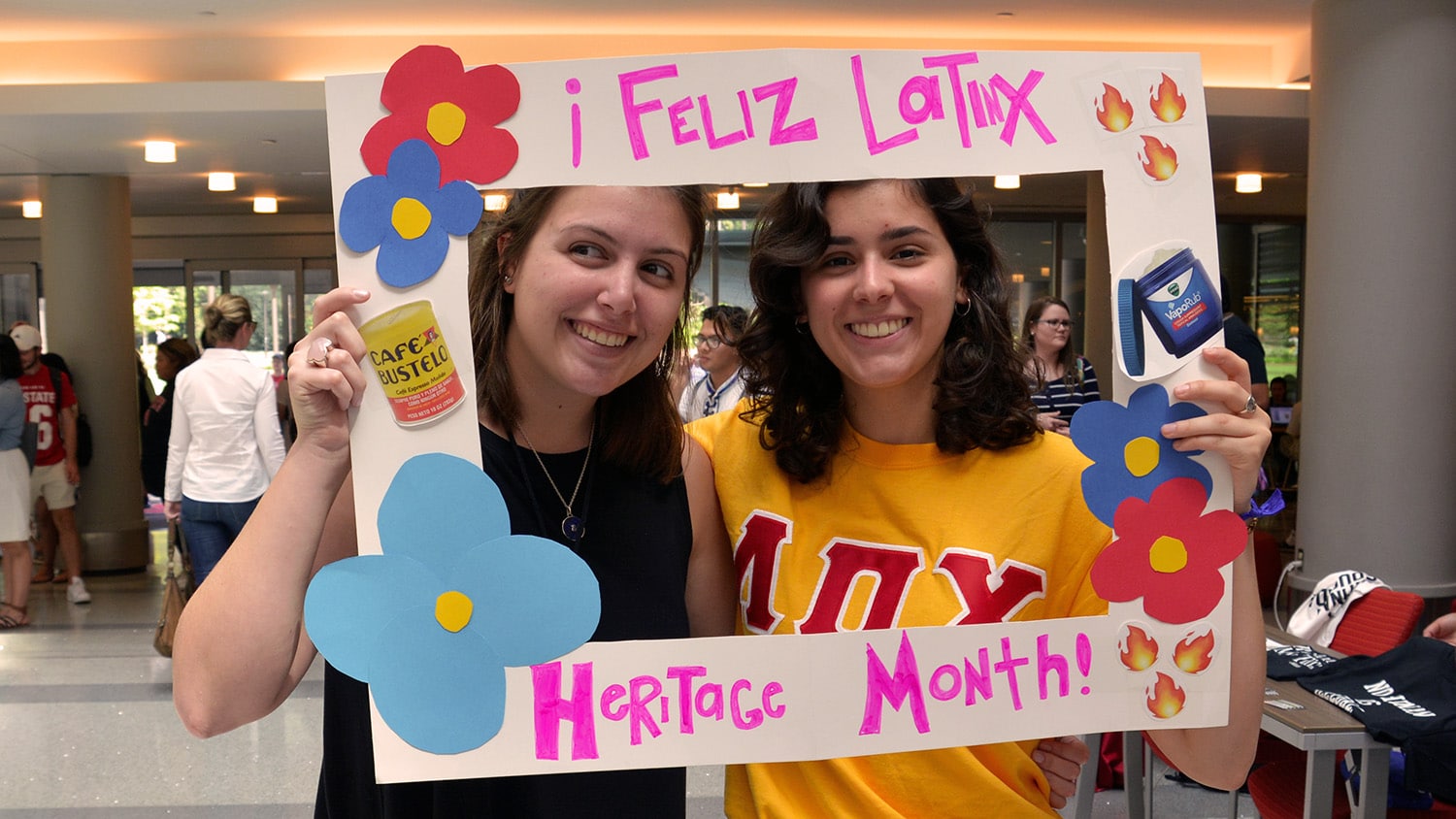 Two NC State students smile in the frame of a cardboard sign that reads "Feliz Latinx Heritage Month."
