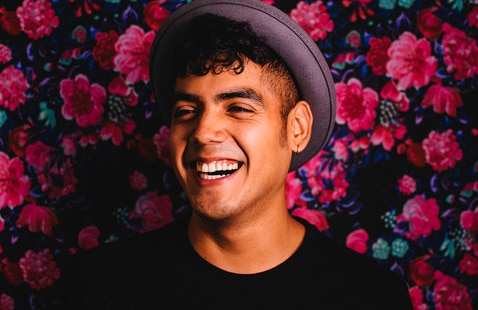 A portrait of NC State Poole College of Management graduate Saul Flores smiling against a floral background.