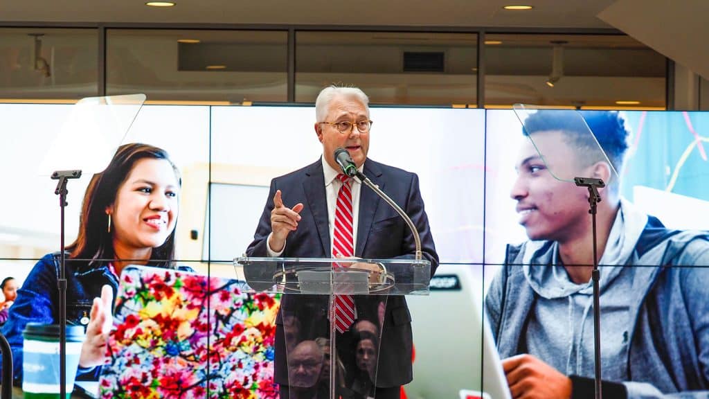 Chancellor Woodson speaks at a podium during his fall address with an image of two students on a video wall in the background.