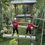 Two students smiling during a ropes challenge course in Schenck Forest.