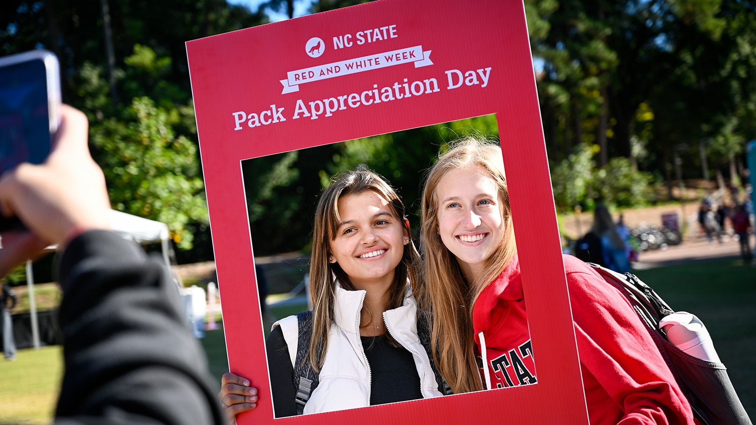 Two students pose for a photo holding a frame with the words "NC State Red and White Week Pack Appreciation Day".