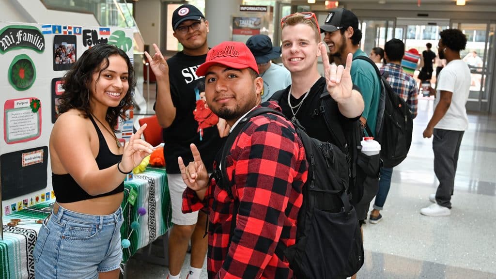 Students make the Wolfpack hand sign at a tabling event for Latinx Heritage Month.