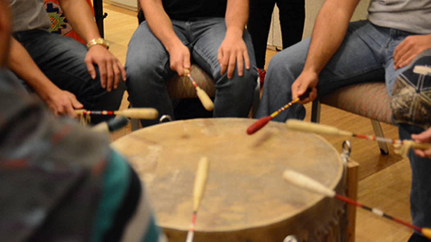 A group of people sit in a circle around a large drum.