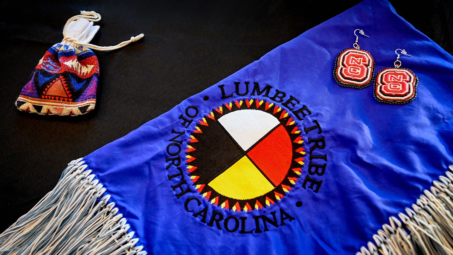 Table decor of a blue Lumbee cloth, NC State beaded earrings, and a colorful cloth pouch.