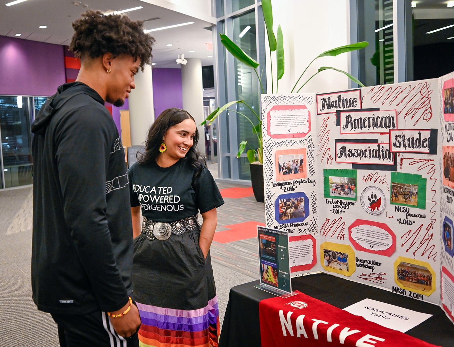 Two students stand together smiling and looking at a poster from the Native American Student Association.