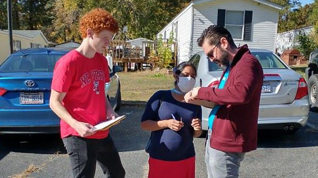 Two people with clipboards talking to a third person