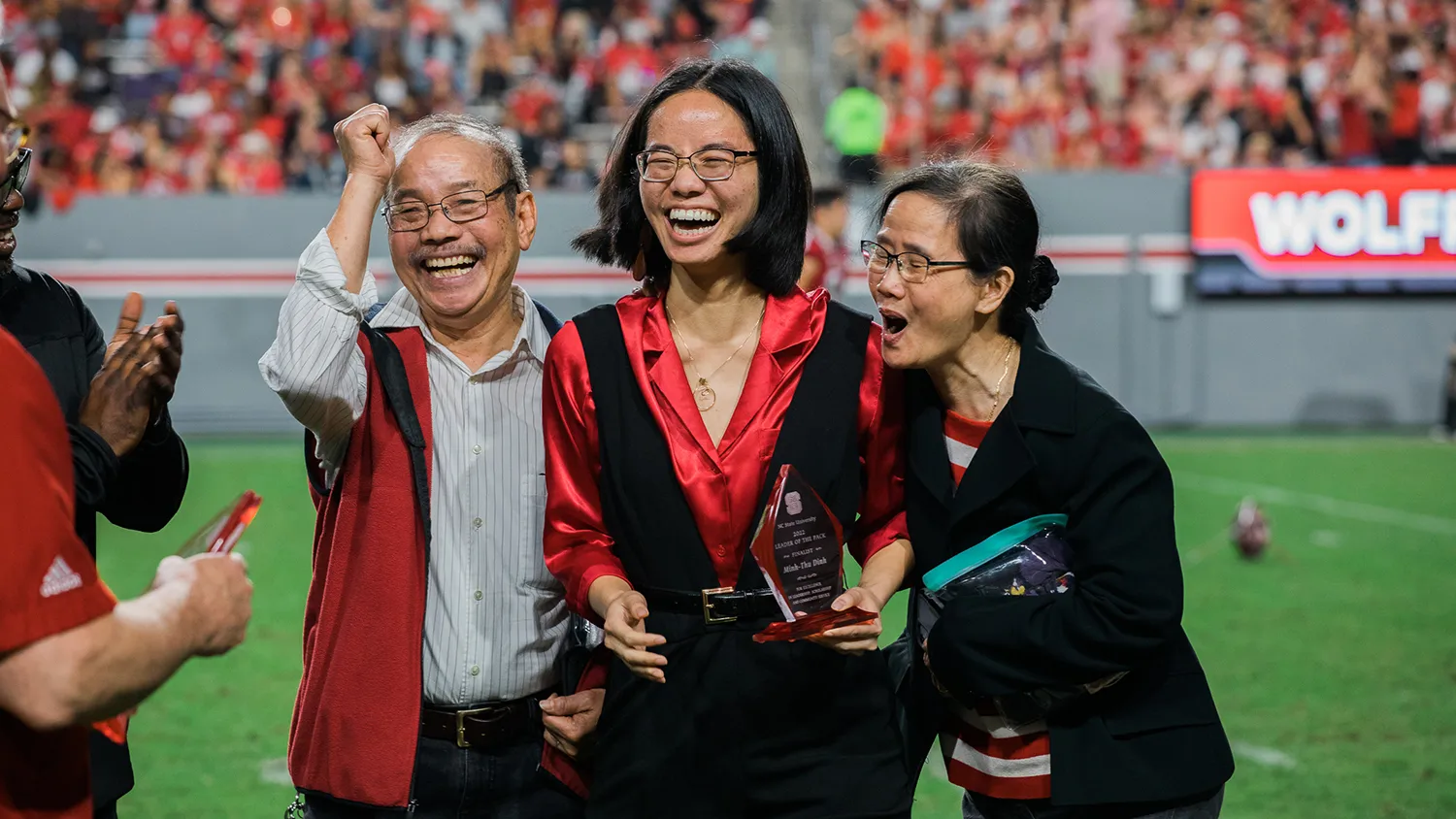 Minh-Thu Dinh stands with family on the football field during halftime to accept the Leader of the Pack award.