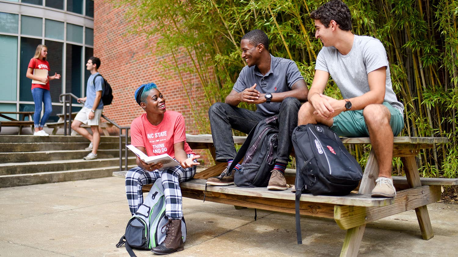 Students talk and laugh while sitting at a picnic table.