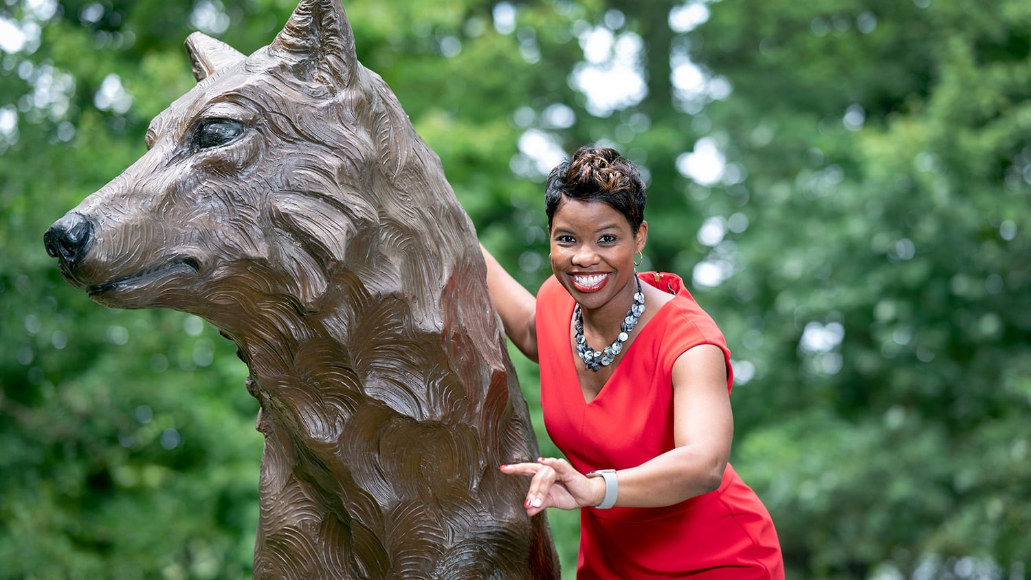 Reshunda Mahone gives the Wolfpack sign next to a bronze wolf statue on campus.