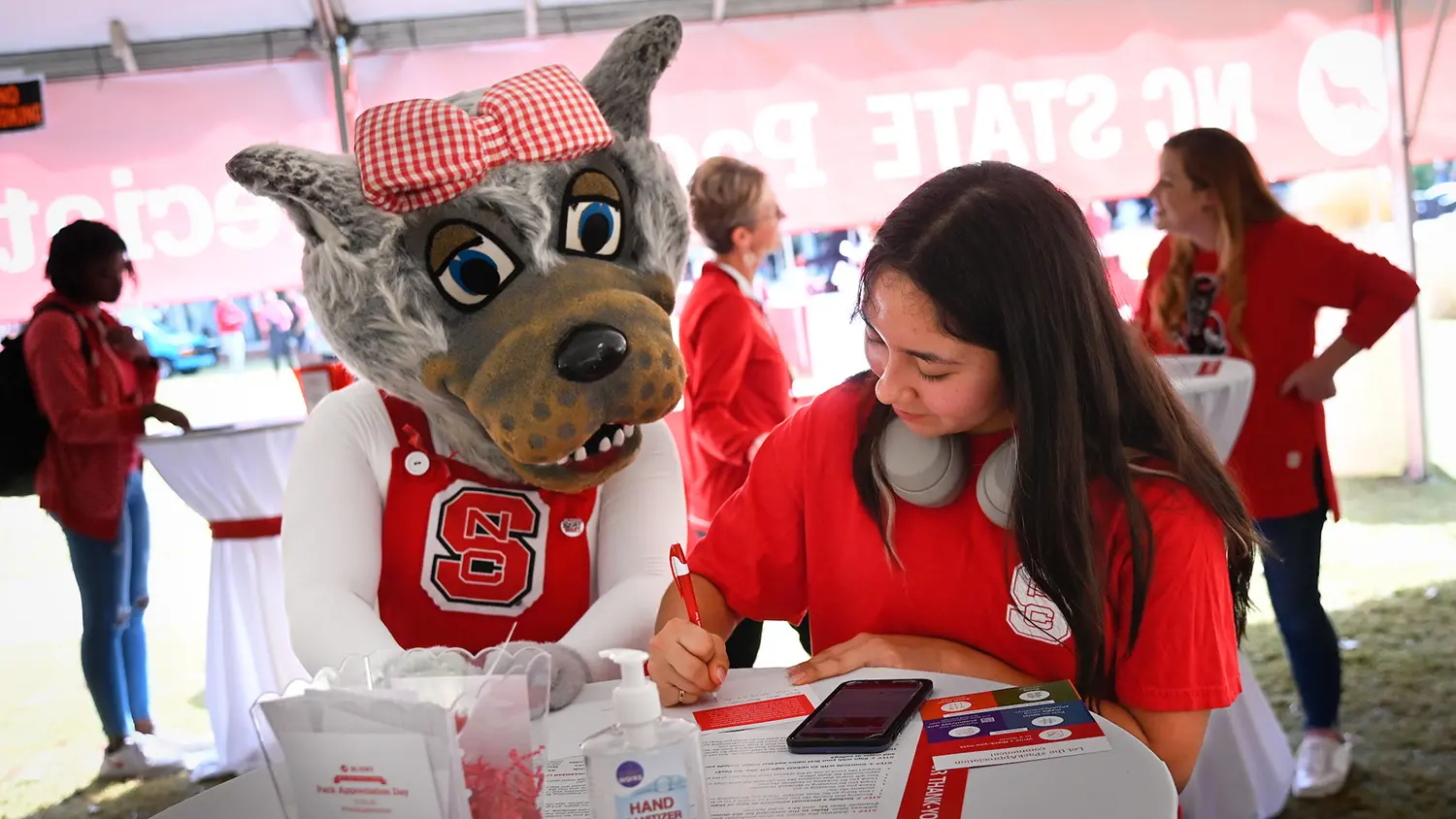 A student sits next to Ms. Wuf while writing a thank-you card.