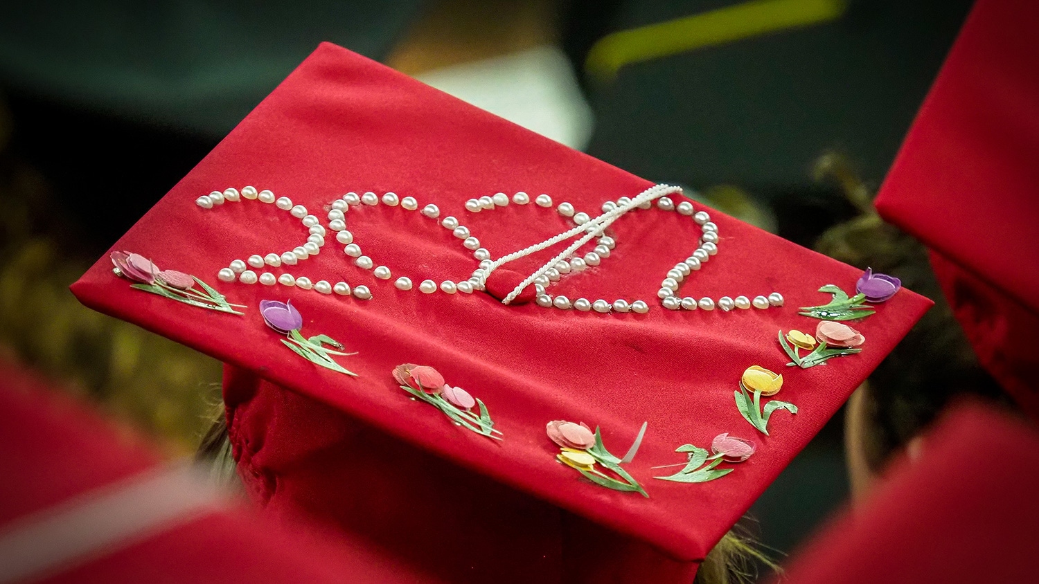 The top of a red graduation cap is embellished with flowers and pearls that spell out "2022".
