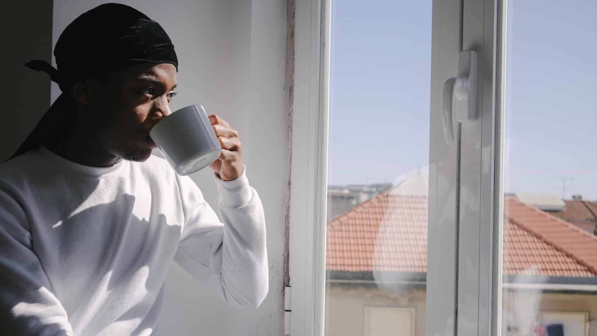 young black man drinks coffee and looks out the window