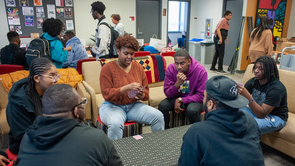Students gather around a table in the African American Cultural Center, each holding playing cards in their hands.