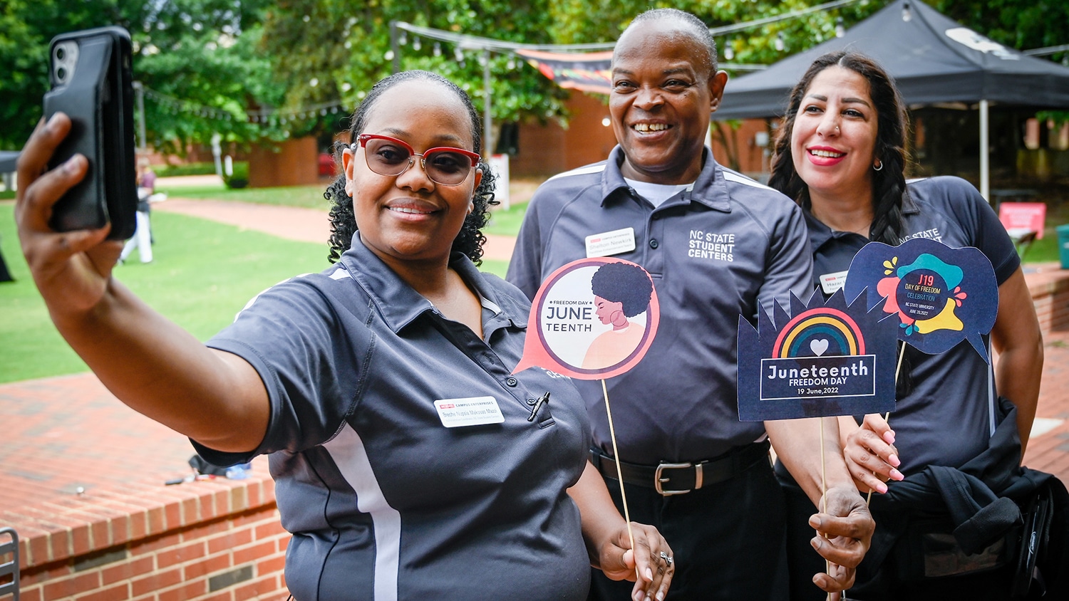 Three employees pose for a selfie at the inaugural Juneteenth celebration. They hold small, colorful Juneteenth signs.