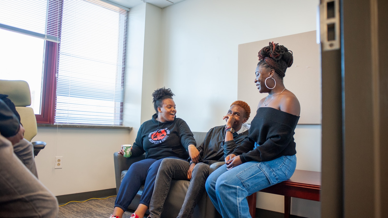 Three students sit together laughing in one of the African American Cultural Center offices.