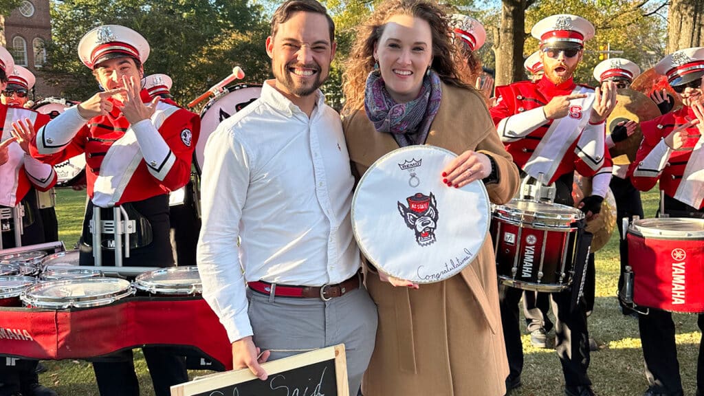 A newly engaged couple poses with NC State's drumline