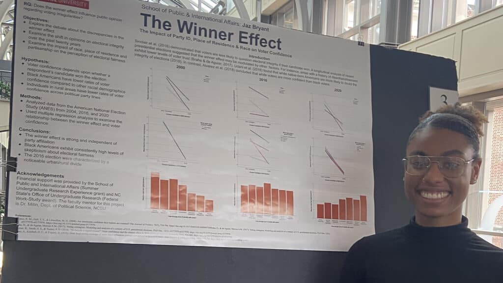 Jaz Bryant smiles in front of her poster presentation at the 2022 State of North Carolina Undergraduate Research and Creativity Symposium.