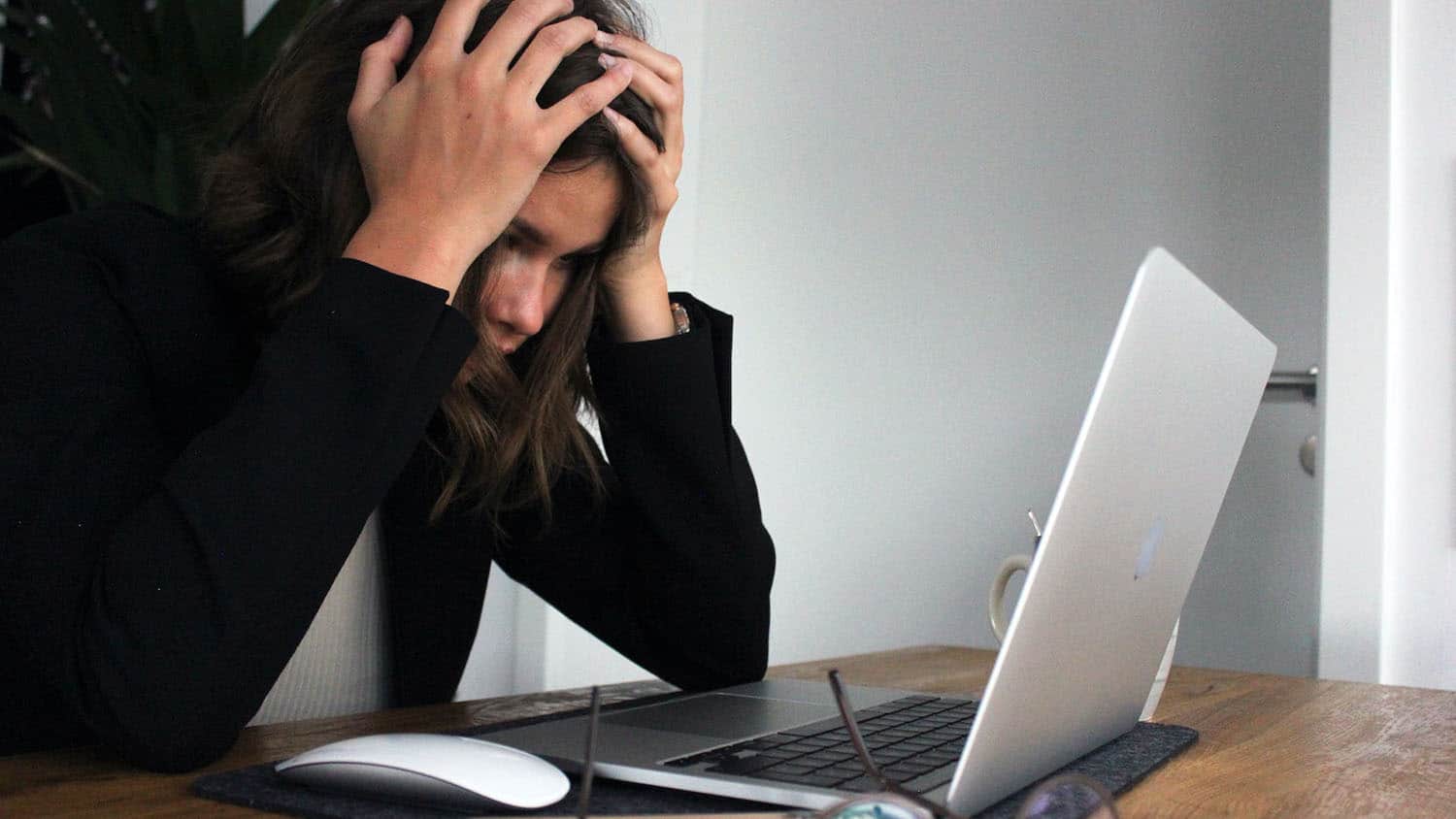 woman looking at laptop screen holds her head in her hands as if stressed