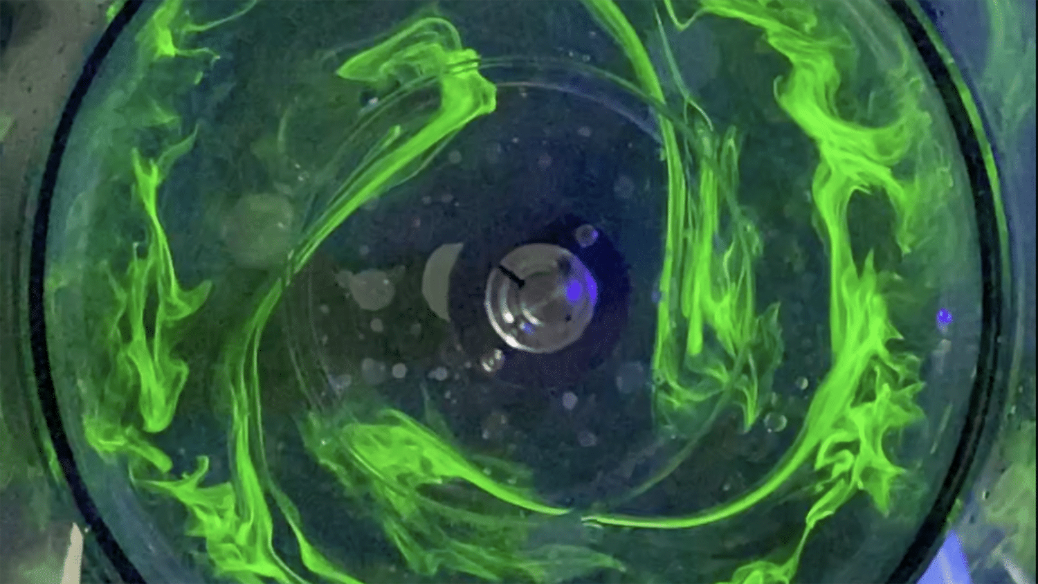 Image shows green fluorescent dye swirling in a water-filled cylinder, part of a student research project supported by the Office of Undergraduate Research.