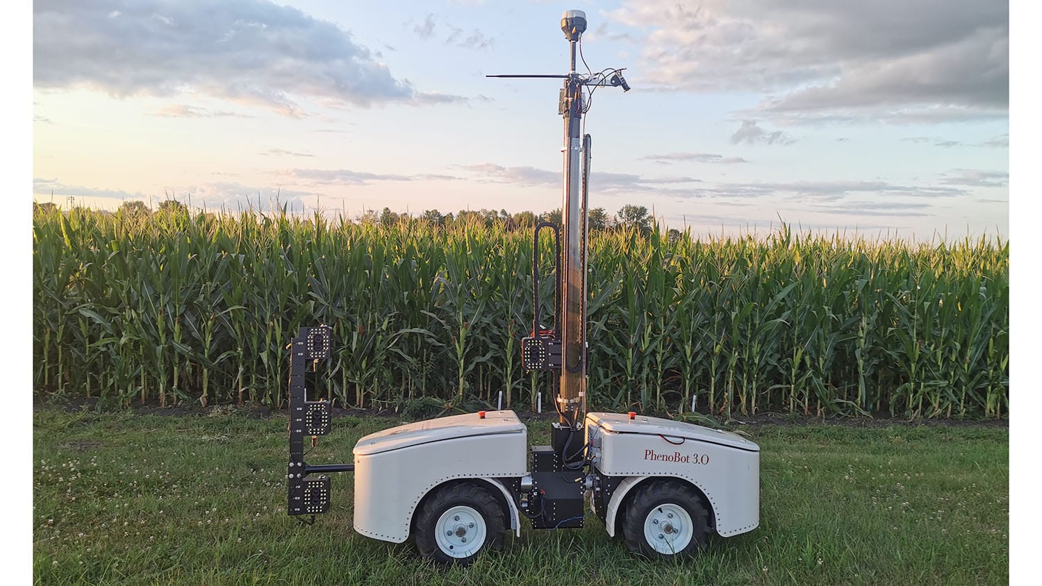 wheeled vehicle contains a tower with multiple tiers of cameras mounted to it. The vehicle is in a corn field.