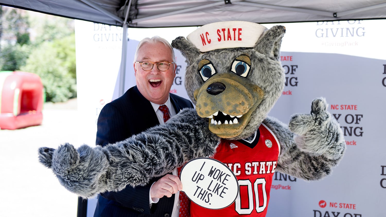 Chancellor Woodson poses for a photo with Mr. Wuf holding a sign that says "I woke up like this" during the 2019 Day of Giving student event