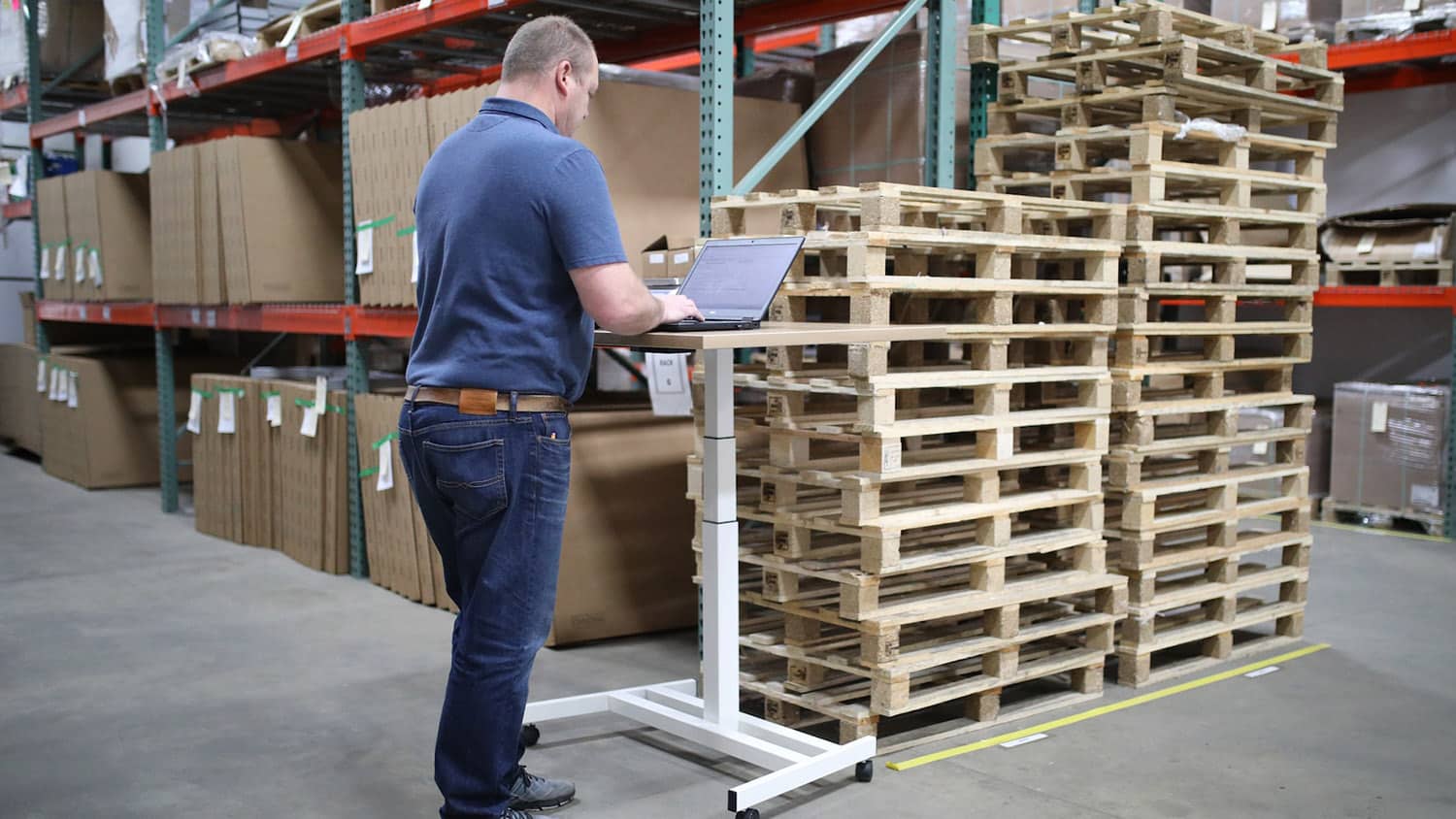 man in a shipping warehouse looks at a laptop computer