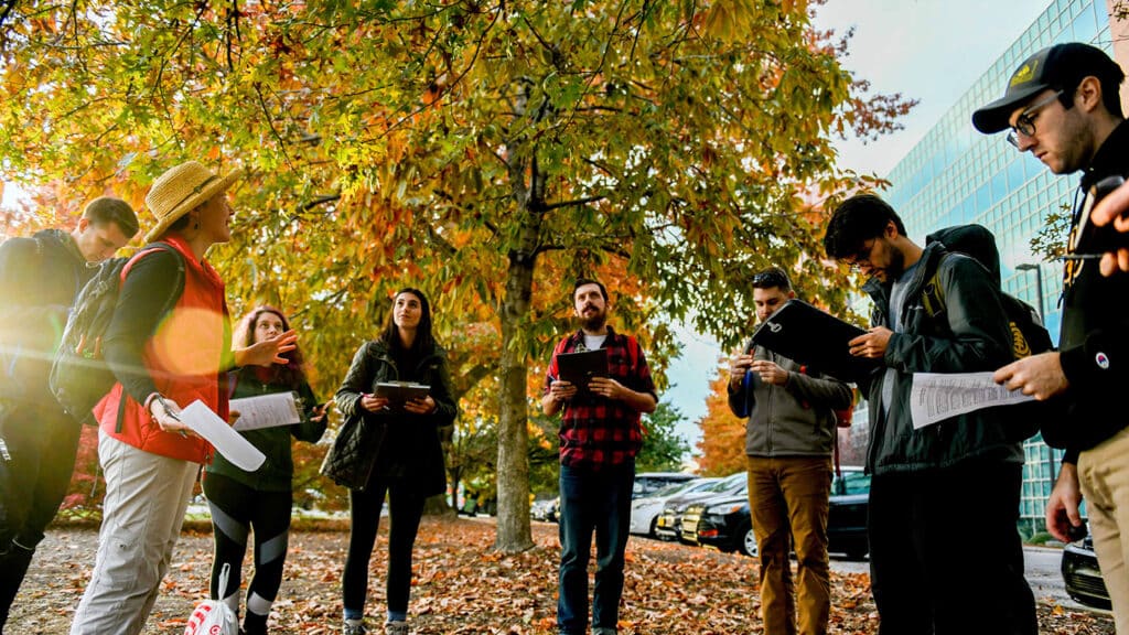 Dr. Steph Jeffries (left) teaches tree identification during a dendrology class outside Jordan Hall on a fall day, with leaves littering the ground nearby.