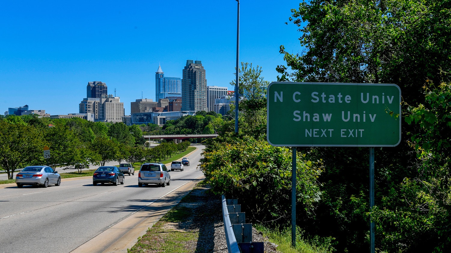 An exit sign marks that NC State University is just minutes from downtown Raleigh's skyline.