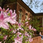 Spring flowers bloom in front of Leazar Hall on a warm, spring day on main campus., as a student rests on a low brick wall in the background.