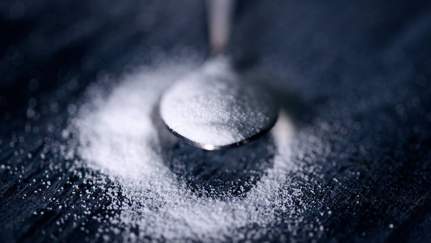 a spoon holds a scoop of white powder over a grey table