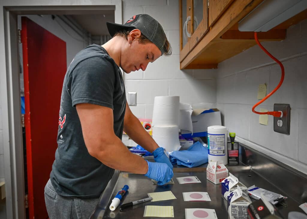 Zach Gabor pipettes milk droplets onto paper-like lab materials. The materials show whether harmful bacteria is detected in the samples.