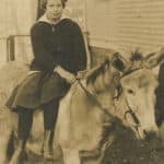 A sepia-toned photo shows a young, school-aged Mary Yarbrough posing side-saddle atop a hinny, an equine hybrid between a female donkey and male horse.