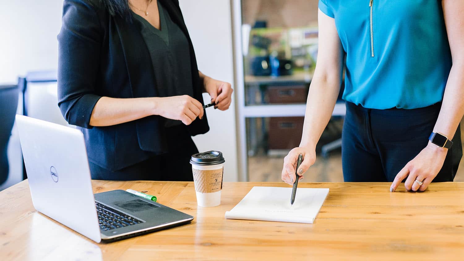 two adults, show from shoulders to waist, stand at a conference table. They appear to be debating something.