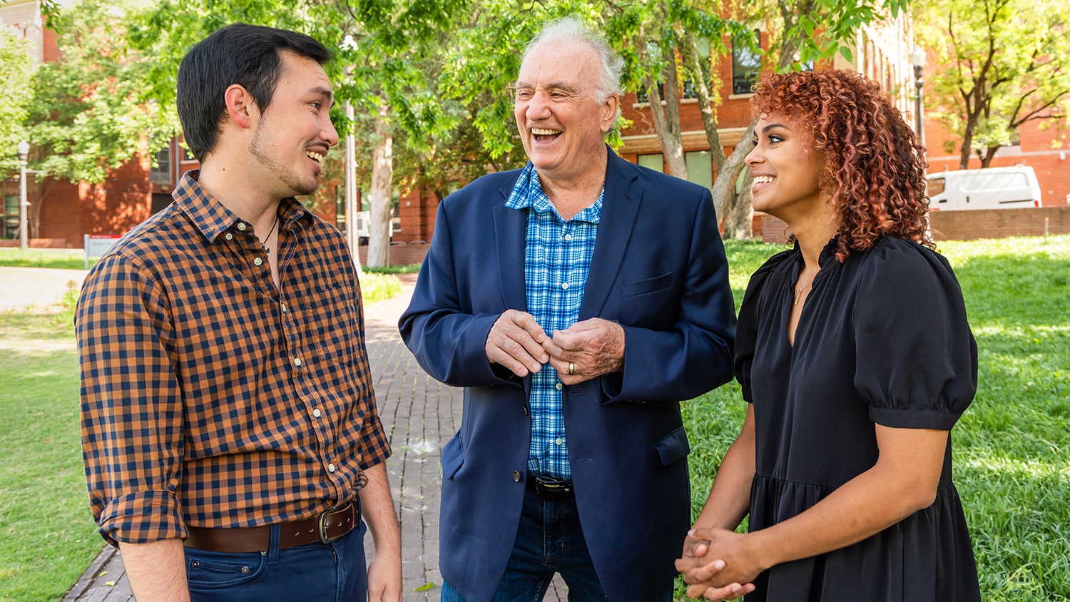 Brody McCurdy, Walt Wolfram and Lydia Elrod stand together and laugh outside Tompkins Hall in the Court of North Carolina.