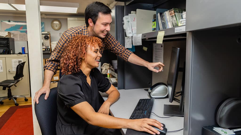 Lydia Elrod sits at a computer while Brody McCurdy looks over her shoulder. The two are working on an oral history about Chatham County.