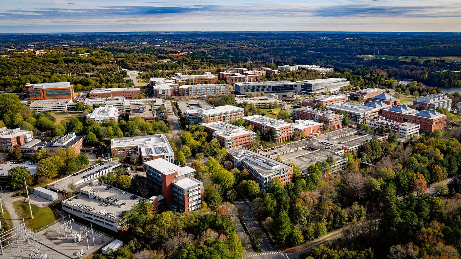 Aerial view of entire Centennial Campus, with trees sprawling to the horizon under a cloudy sky in the background.