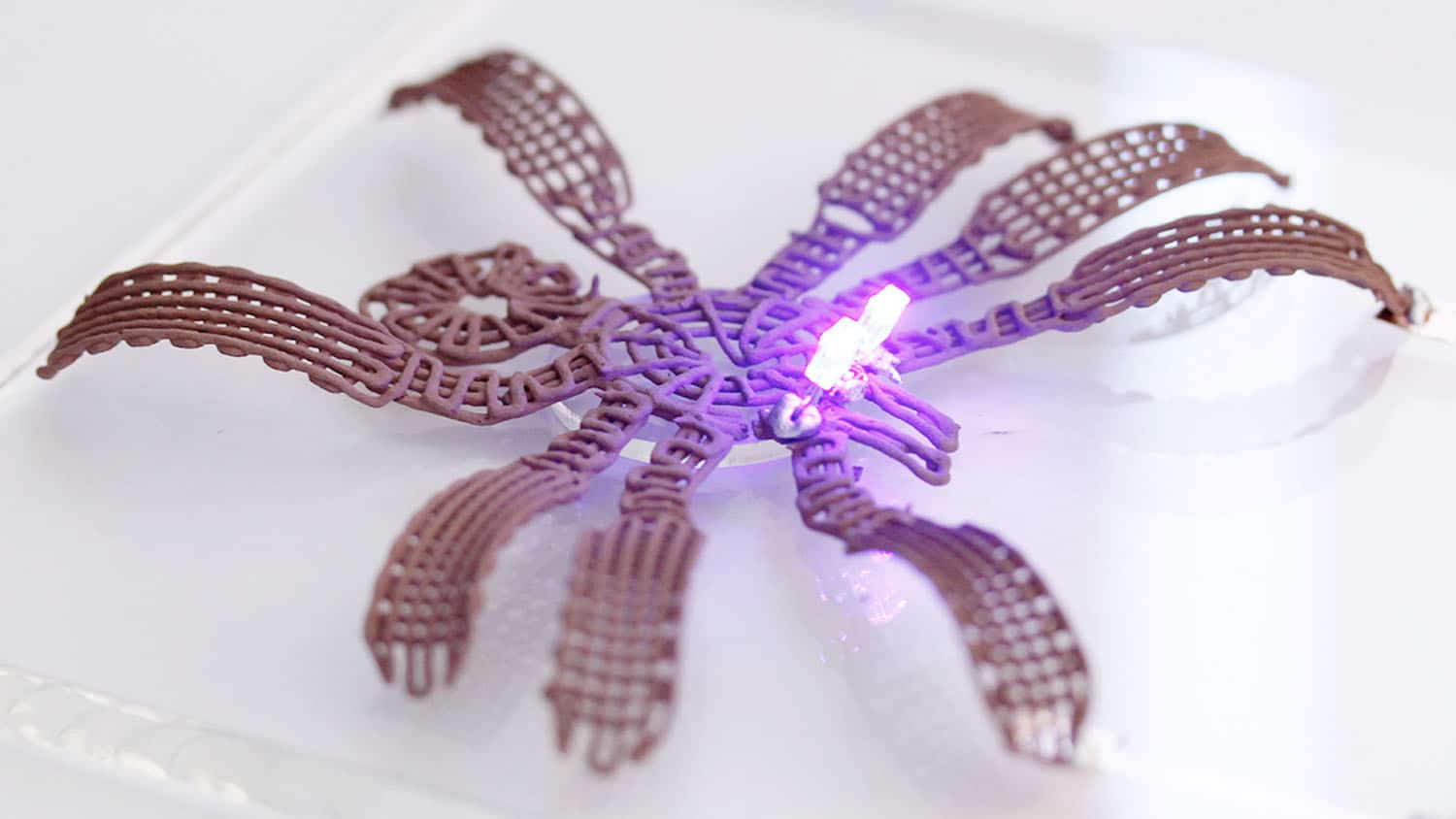 a metallic spider sits on a white table. the spider has a glowing LED on its head