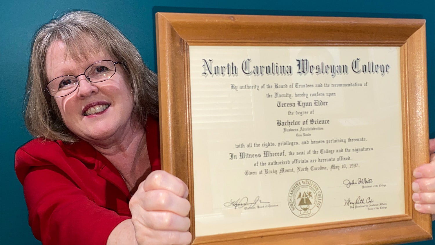 Teresa Benjamin holds up her golden-framed diploma from North Carolina Wesleyan College