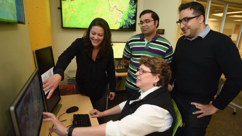 Georgina Sanchez, a research scholar with the Center for Geospatial Analytics, points at a screen while demonstrating a point to other researchers in the Geospatial Analytics Lab.
