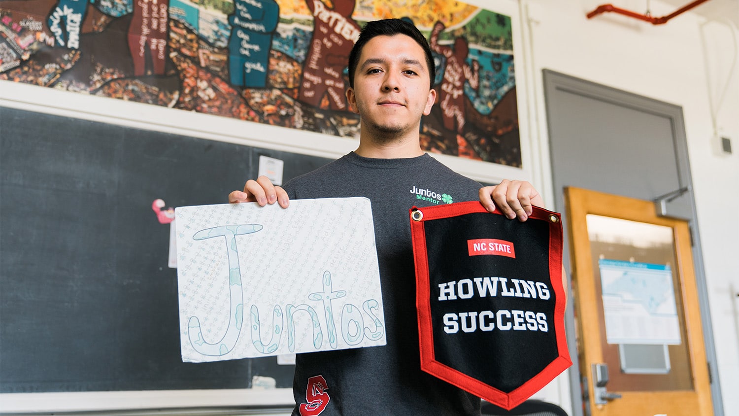 Sebastian Rios holds up a handwritten sign that reads "Juntos" and a red and black pennant that reads "Howling Success."