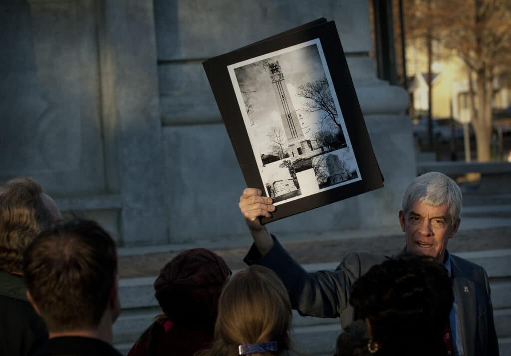 Tom Stafford holds up black and white prints of photos of the Belltower in front of a tour group