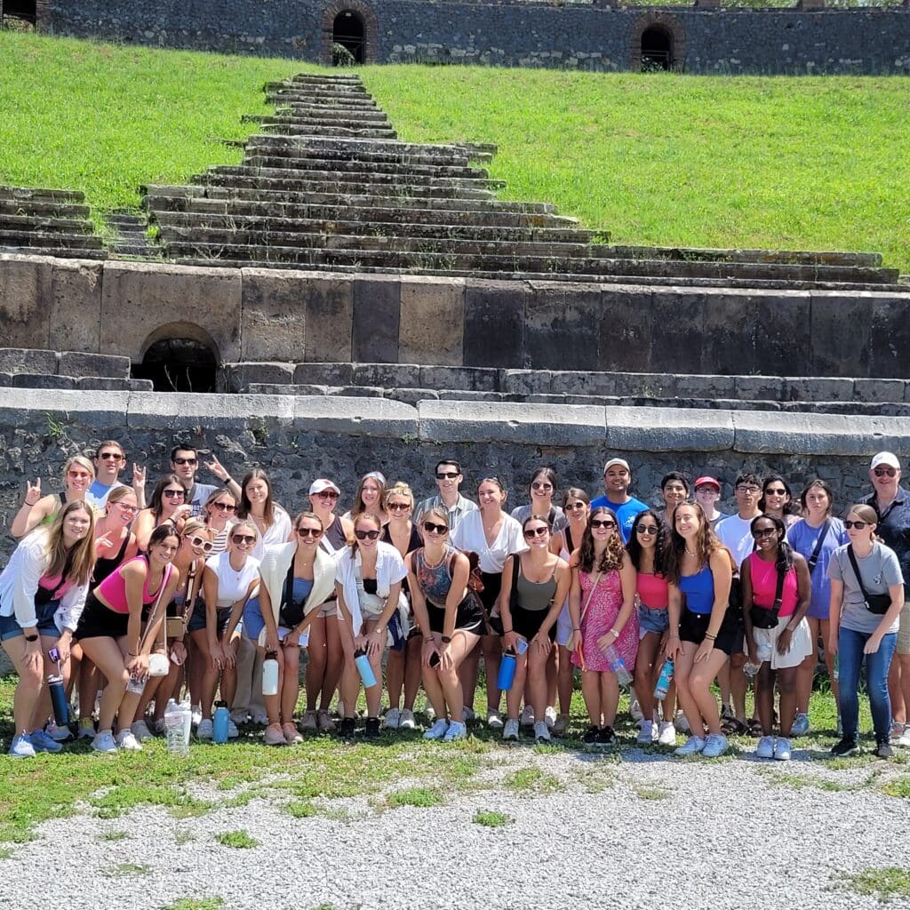 A large group of students standing in front of an ancient stone staircase on a grassy hill