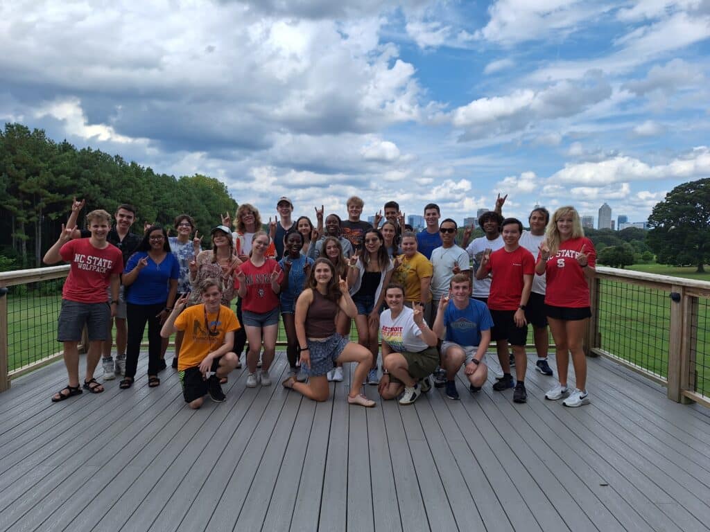 A group of Honors Program students pose on a wooden deck in Dix Park and make wolfie signs