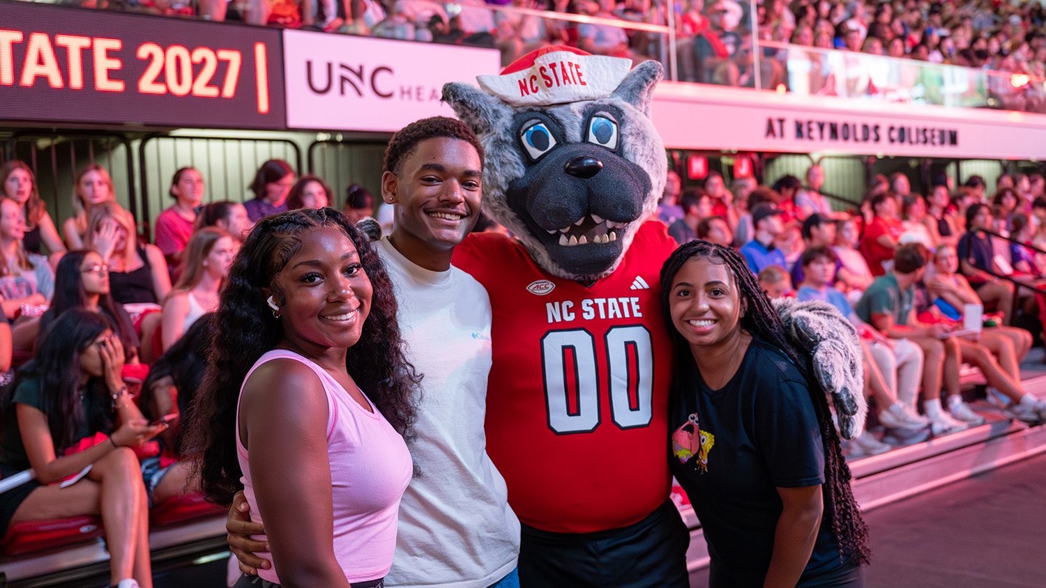 Three students pose for a photo with Mr. Wuf during new student convocation in Reynolds Coliseum.